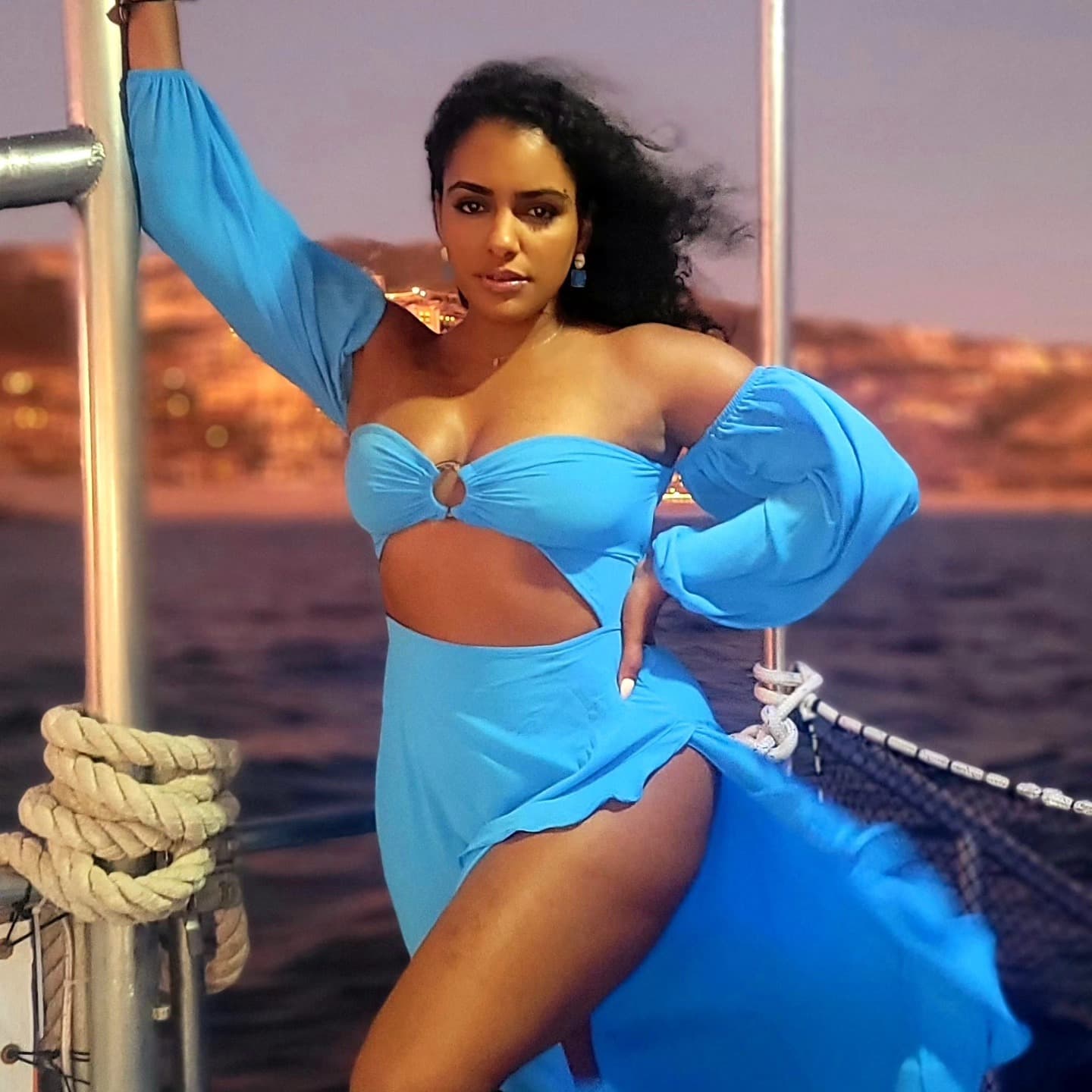 Woman in a vibrant blue cut-out dress posing on a boat deck at night.