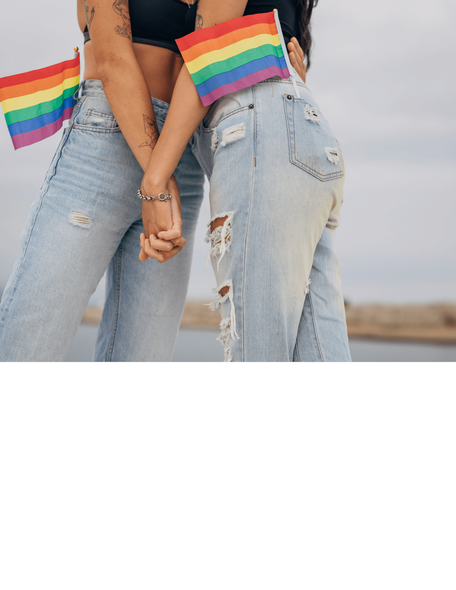 Two people in ripped jeans hold hands, each with a small rainbow pride flag.
